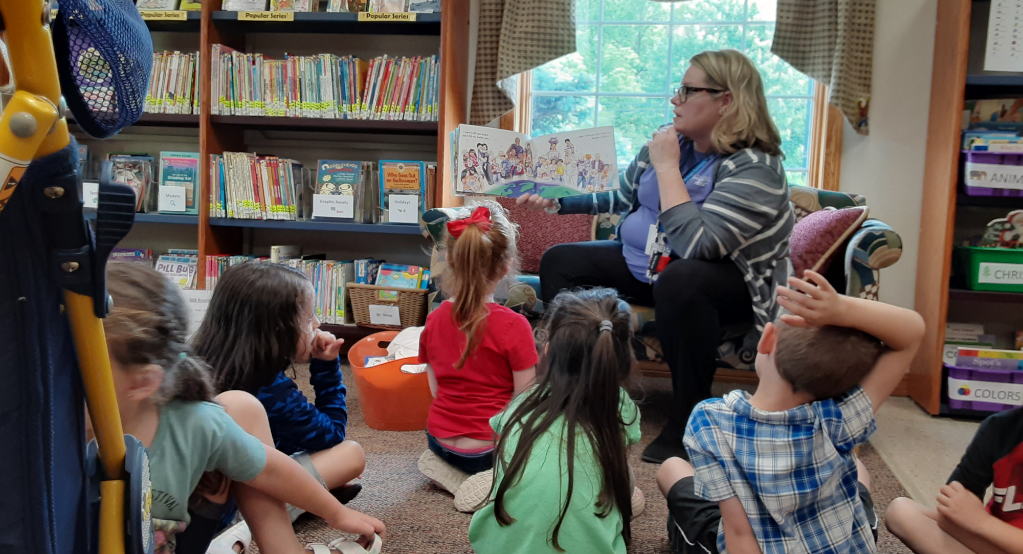 A storyteller reads to captivated children in a library, surrounded by books and colorful resources.