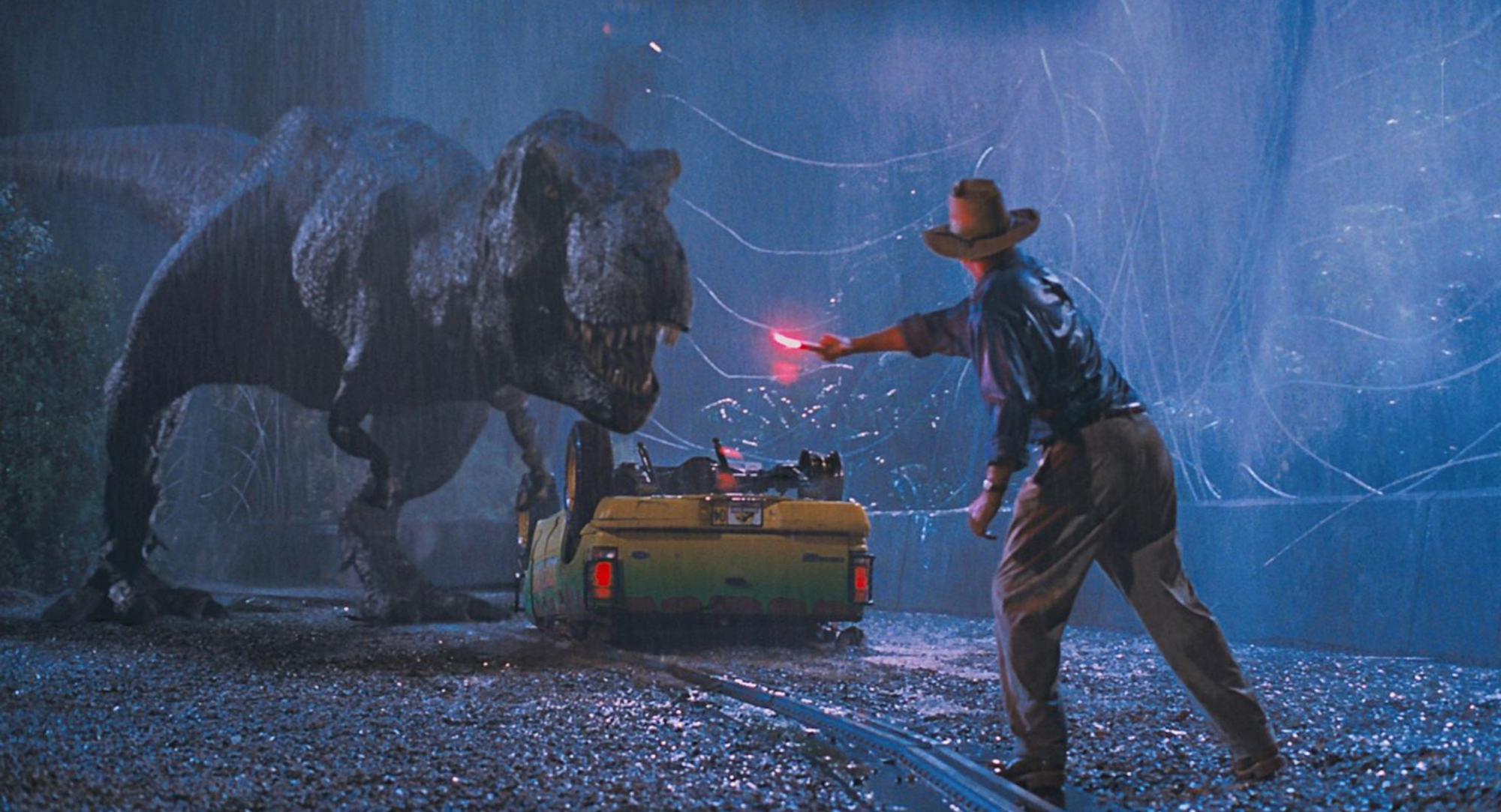 A person confronts a large dinosaur in the rain, while a partially flipped vehicle is in the background. Tension is high.