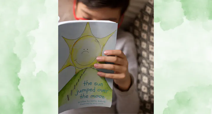 A child reads "The Sun Jumped Over the Moon," a book illustrated with a cheerful sun and a grassy hill.