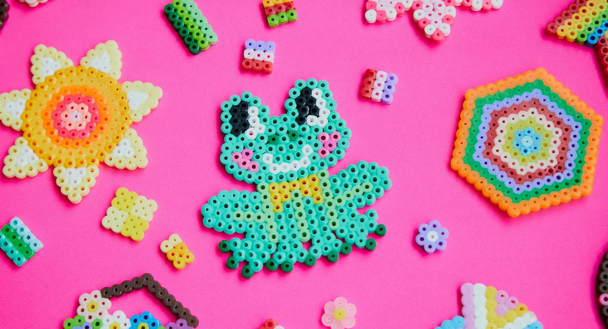Colorful bead art pieces include a frog, a sun, and various shapes on a bright pink background.