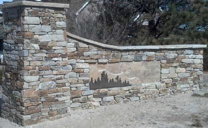 Stone wall with a faded mural, surrounded by dry vegetation.