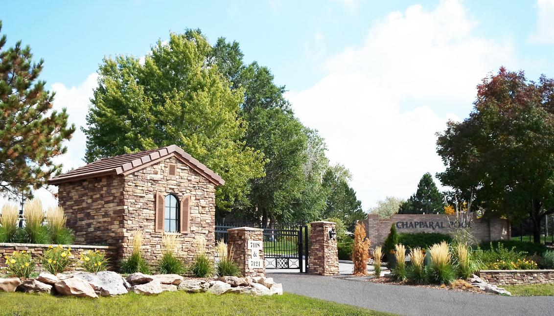 Entrance to "Chapparal" with stone structures, iron gate, landscaped garden, and trees.