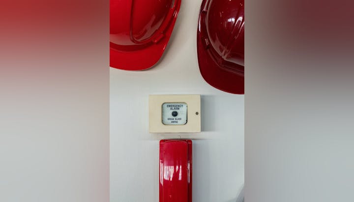An emergency alarm button with instructions "BREAK GLASS" and two red hard hats above it.
