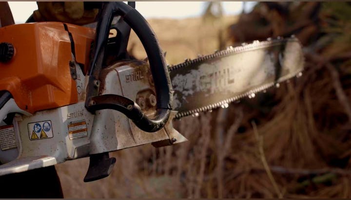 A close-up of a STIHL chainsaw with a blurred natural background.
