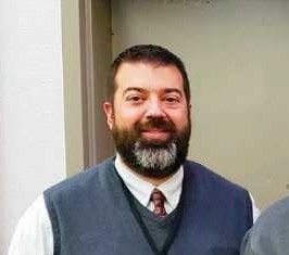 A smiling bearded man in a vest and tie.