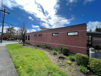 Brick building with small windows, surrounded by grass and shrubs, under a partly cloudy sky at an intersection.