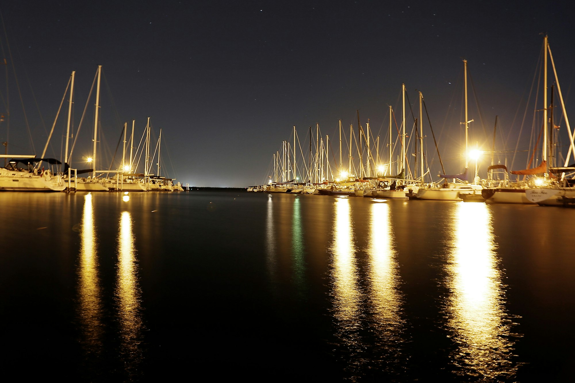 A tranquil night scene of a marina with illuminated boats and reflections on calm water.
