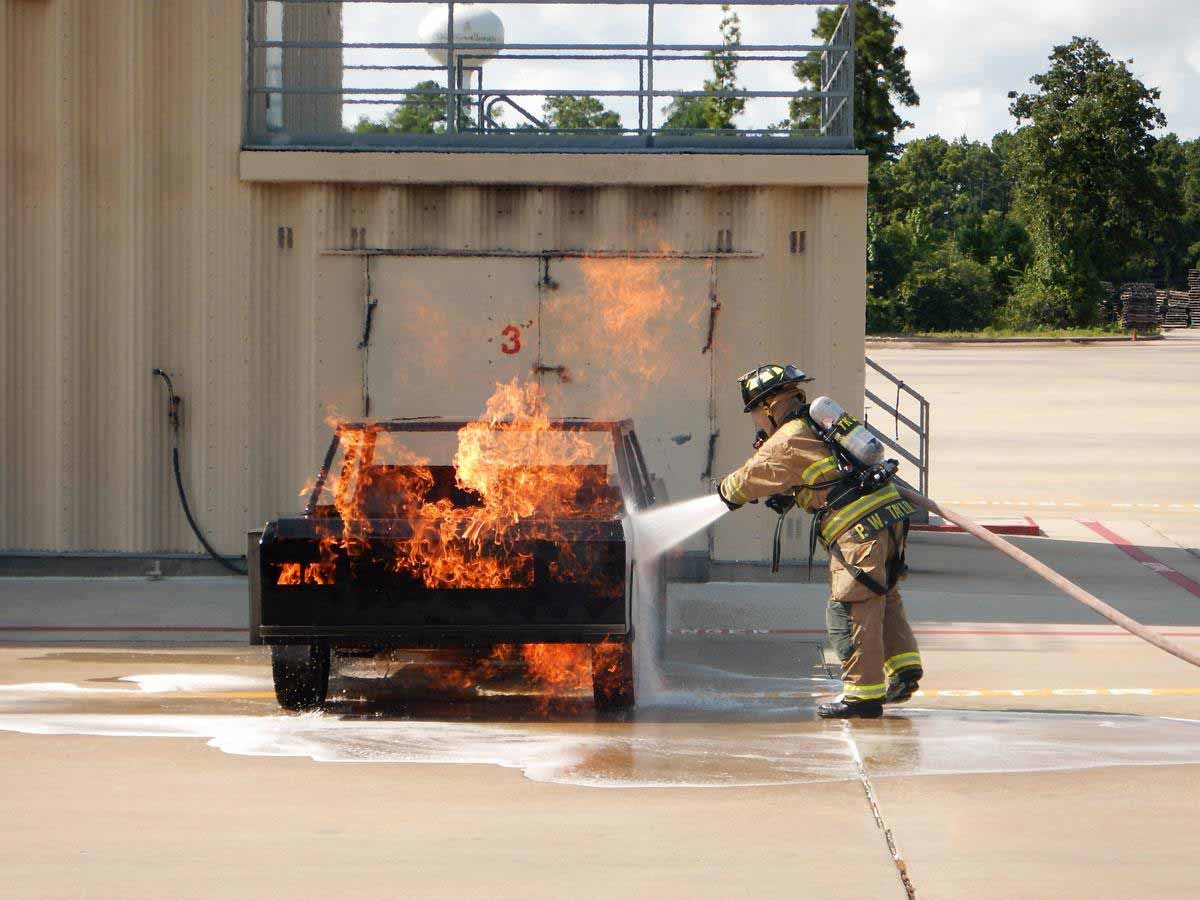 A firefighter is extinguishing a burning mock-up vehicle during a training exercise.
