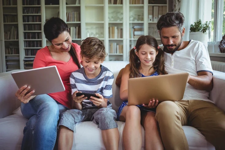 A family of four using digital devices together on a couch.