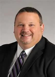 A smiling man in a suit with a striped tie.