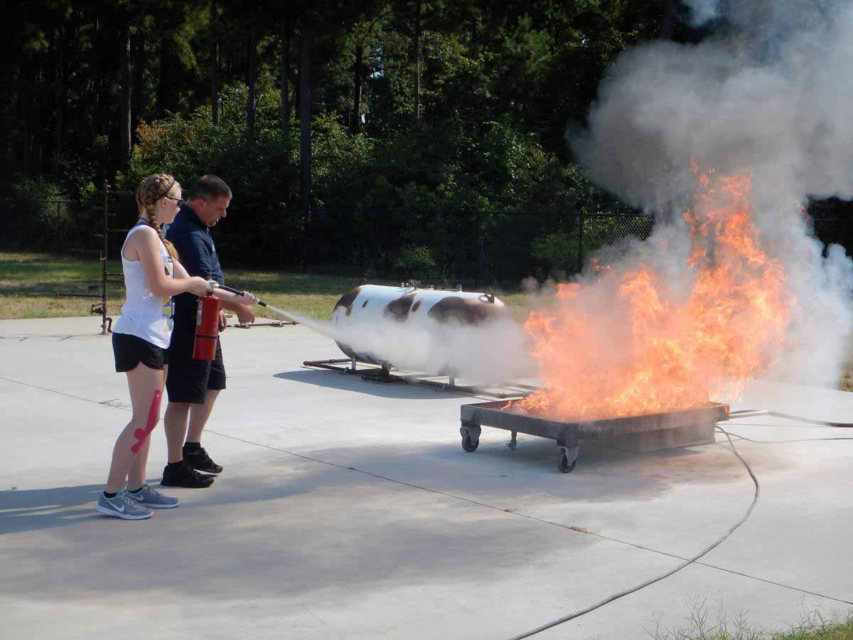 Two people using a fire extinguisher on a training fire.