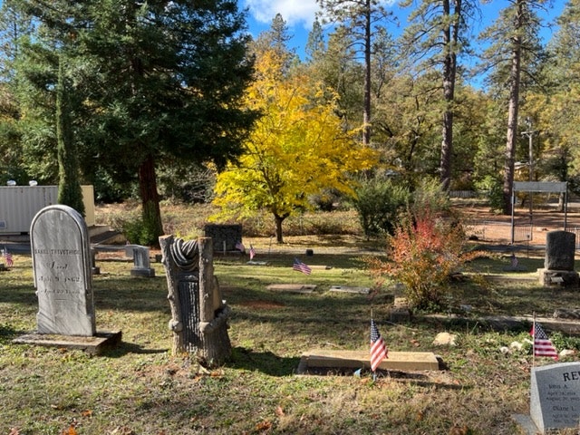 A peaceful cemetery with grave markers, autumn trees, and American flags.
