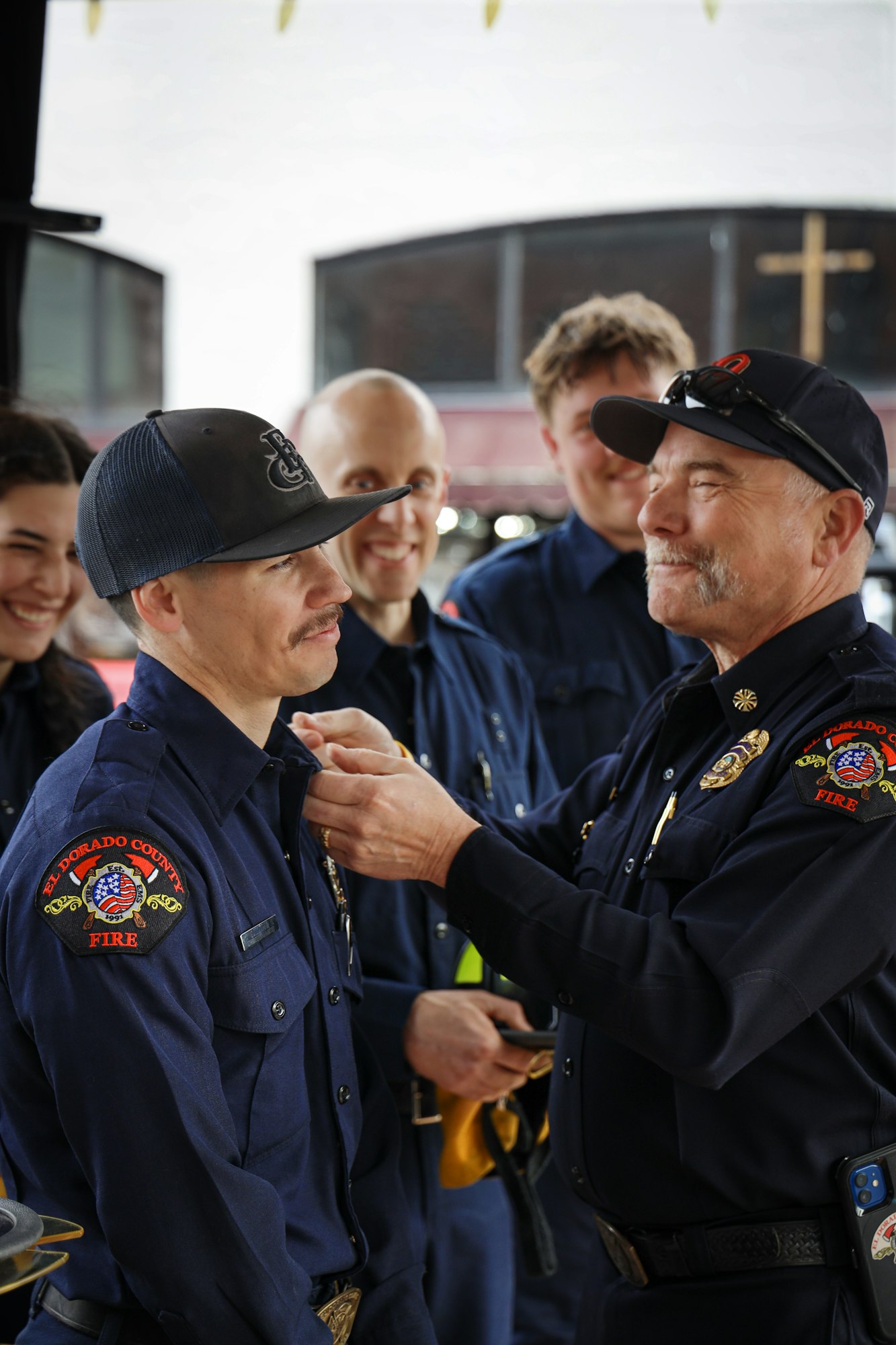 A group of firefighters shares a light moment as one is being pinned or recognized, showcasing camaraderie and teamwork.