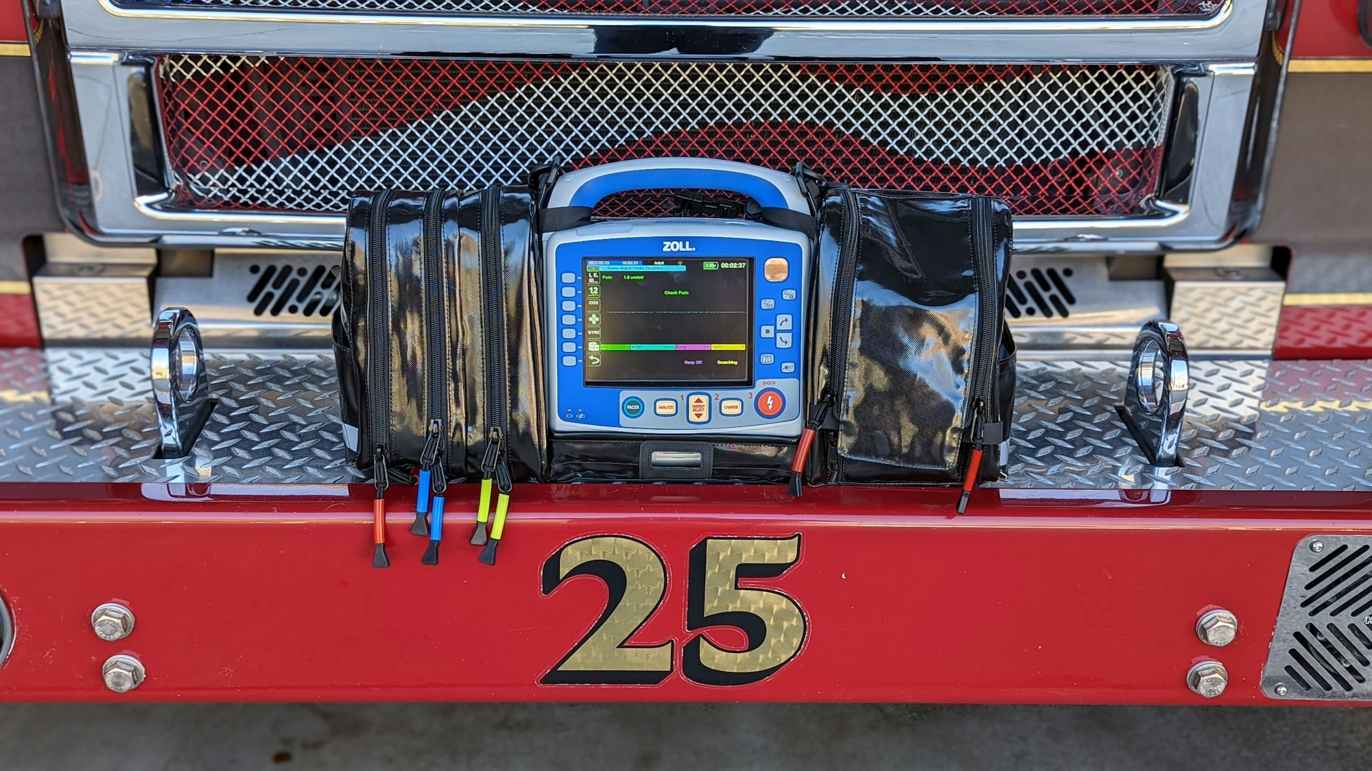 contains numbers 25, red bumper, chrome, diamond plate, monitor defibrillator with blue boarder and black fabric case