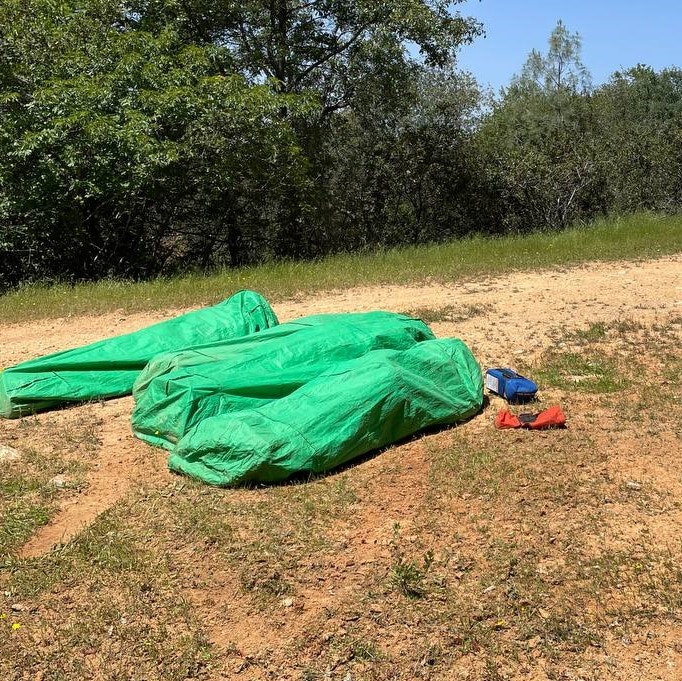 The image shows several green tarps laid on the ground, with some smaller items nearby, set in a natural, grassy area.