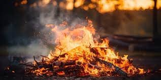 A campfire with flames and glowing embers, surrounded by darkness.