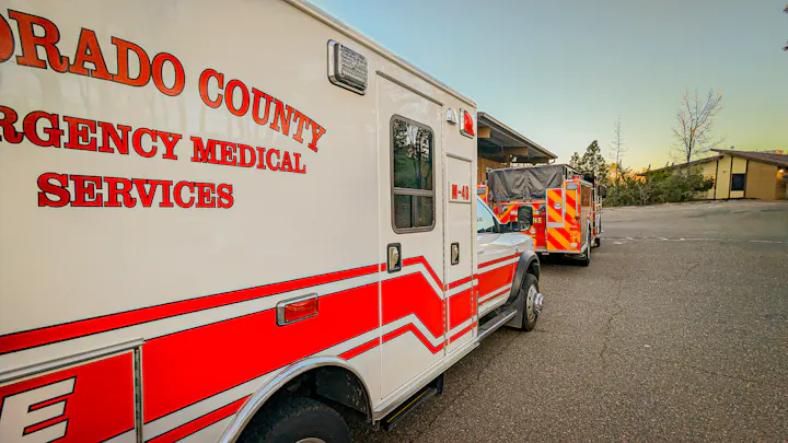 The image depicts emergency service vehicles parked in a lot, including an ambulance and a fire truck.