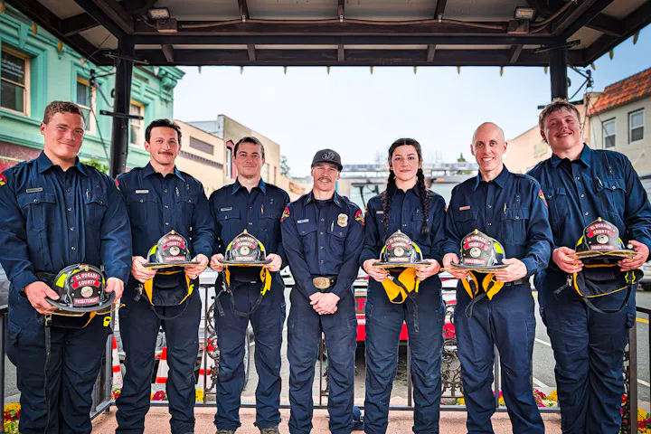 A group of six firefighters in uniform stands together, holding helmets marked "El Dorado County Probationary."