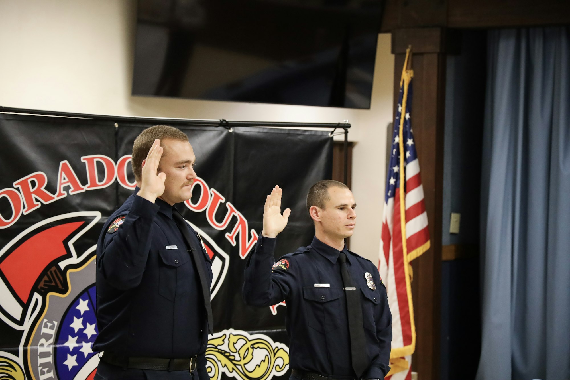 Two firefighters taking an oath with a US flag and department banner in the background.