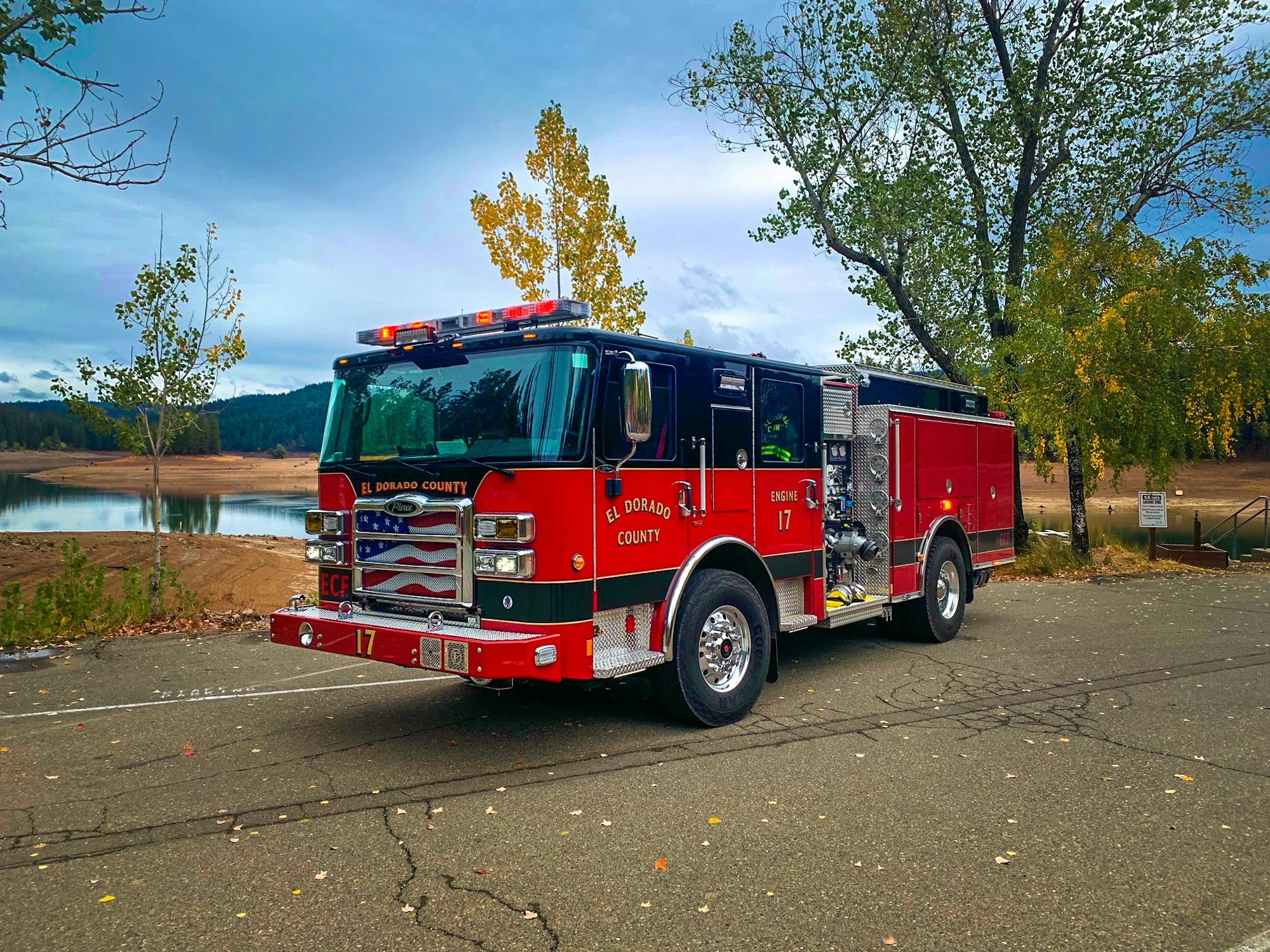 A red fire engine from El Dorado County parked near a lake, surrounded by trees and under a cloudy sky.