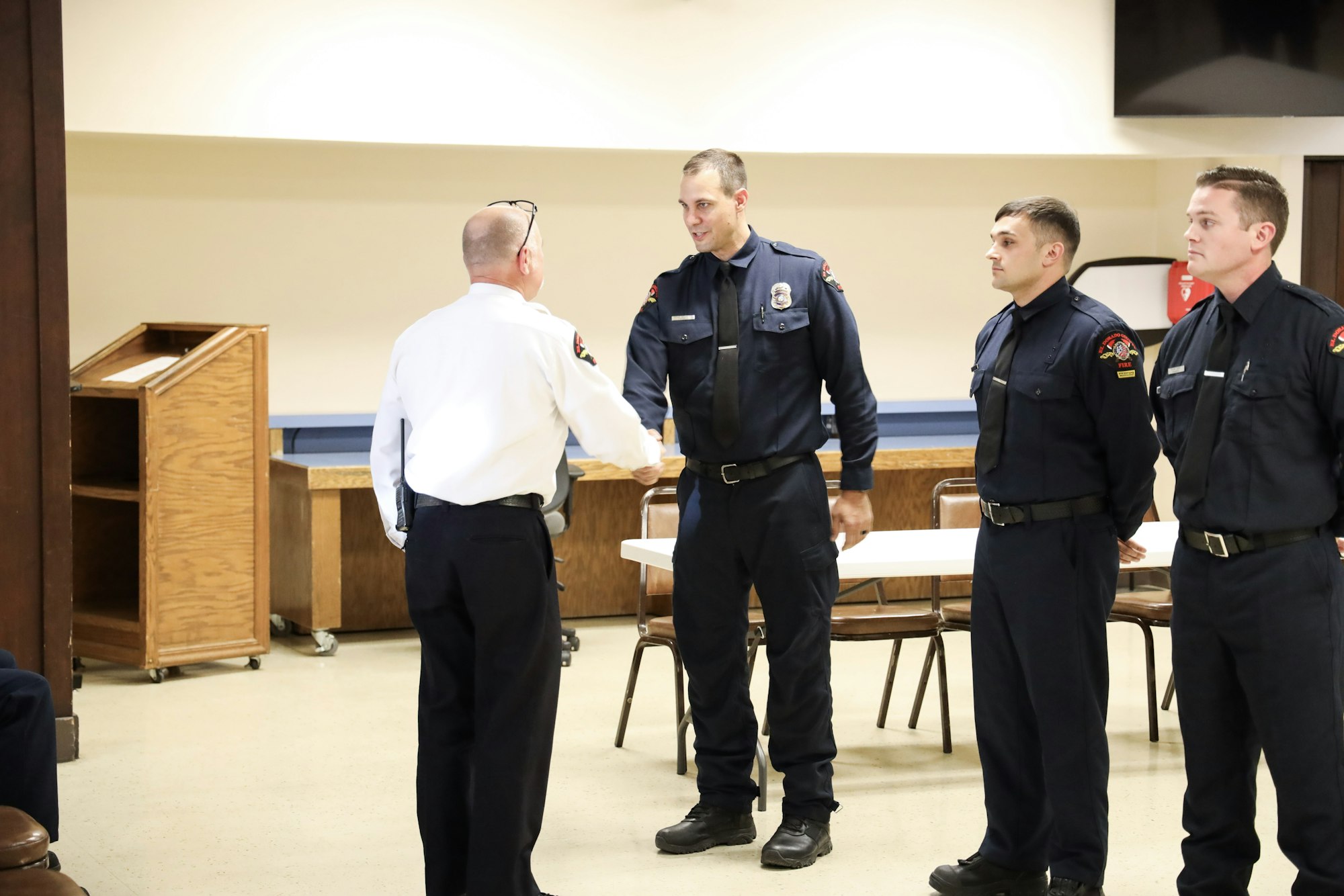 Four uniformed men, one shaking hands, in an indoor setting, possibly during a ceremony or a meeting.
