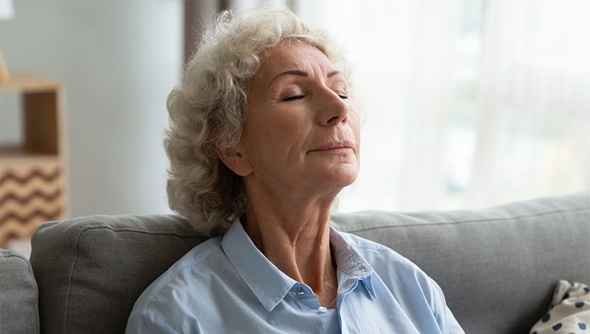 A serene elderly woman with closed eyes, relaxing on a sofa.