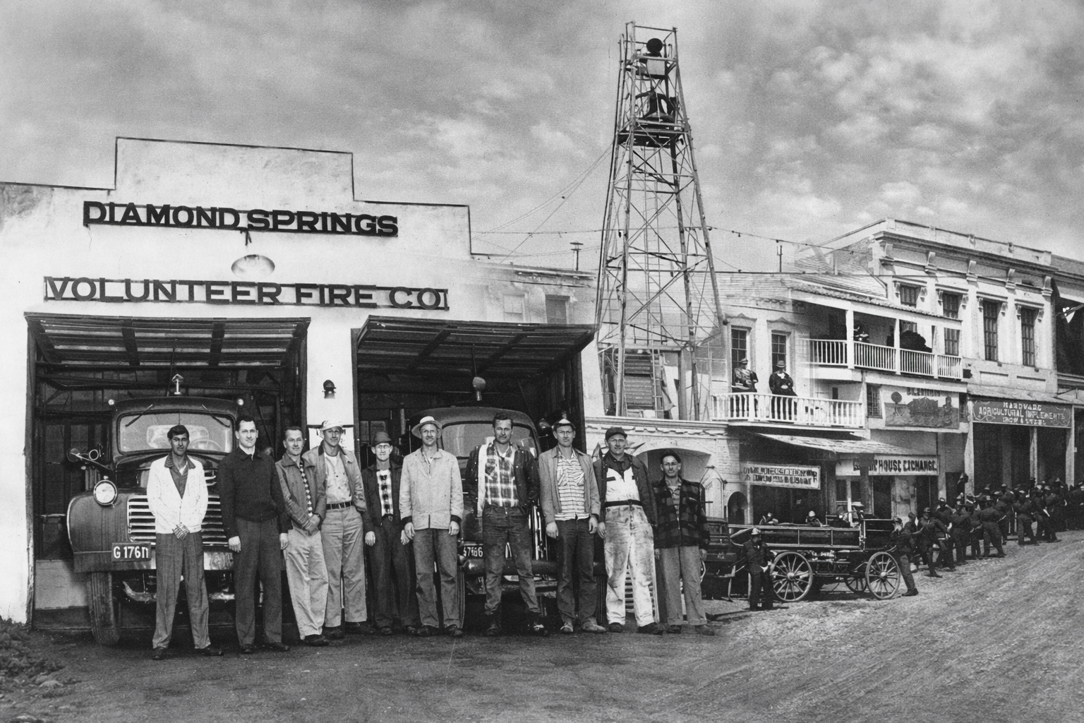 A historical photo of volunteer firemen posing outside their station in Diamond Springs, with fire trucks and a tall lookout tower.