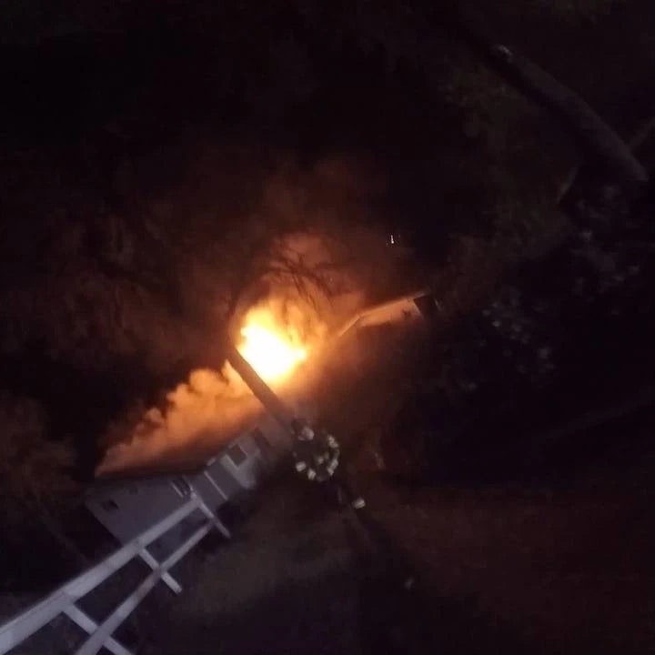 contains fire in the distance, firefighter approaching, white board fence, building on fire