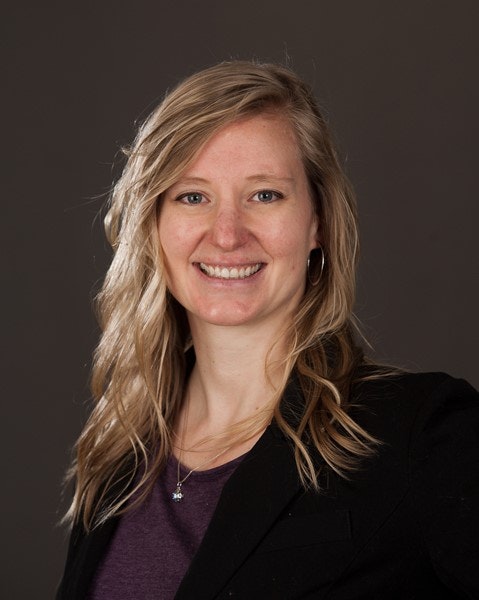 Smiling woman with blonde hair, wearing a black blazer and purple shirt, professional headshot.