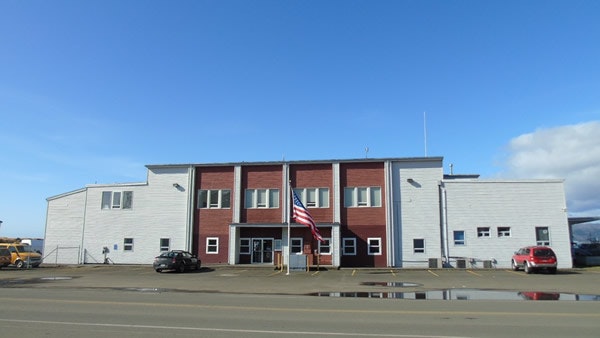 A two-story building with American flag, cars parked outside, under a blue sky with clouds.