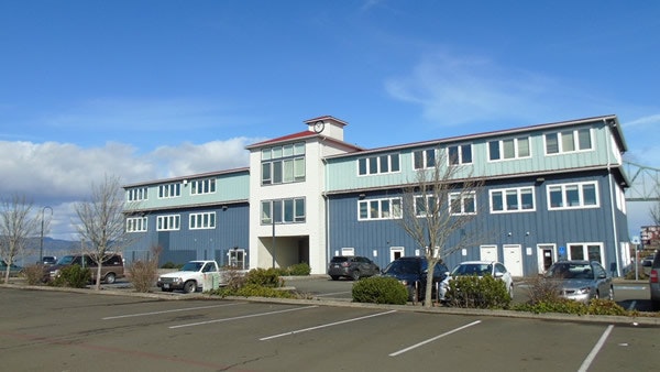 A blue two-story building with parking in front and a partly cloudy sky above.