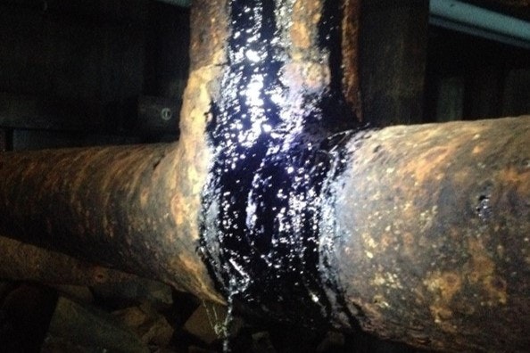 Rusty pipes with black substance leaking at a joint, possibly oil.