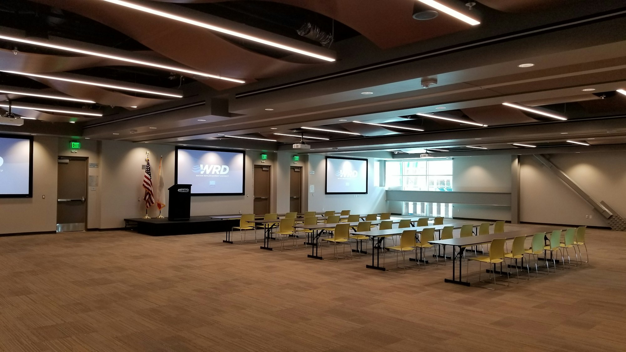 Empty conference room with rows of yellow chairs, tables, screens displaying "WRD," a podium, and a flag.