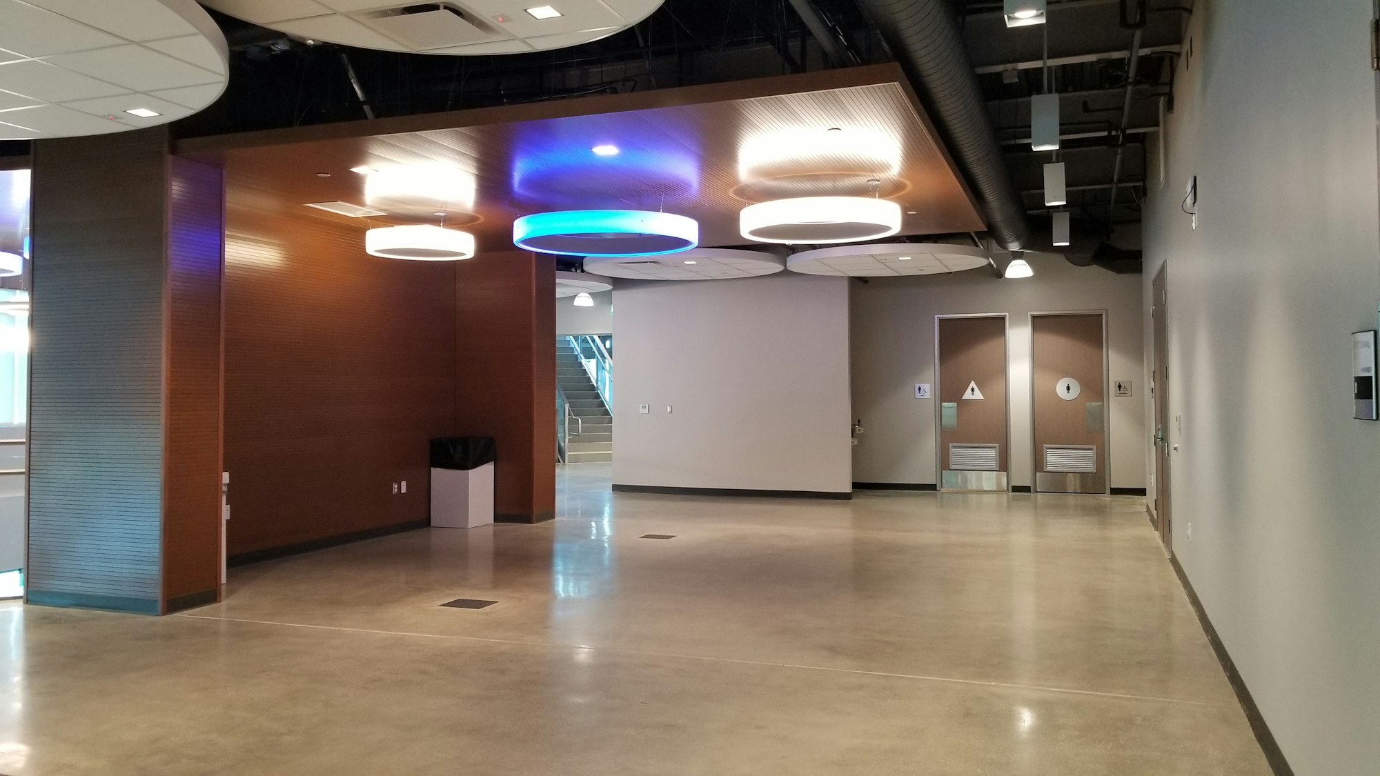 Modern interior with circular ceiling lights, brown walls, stairs in the background, and restroom signs on doors.