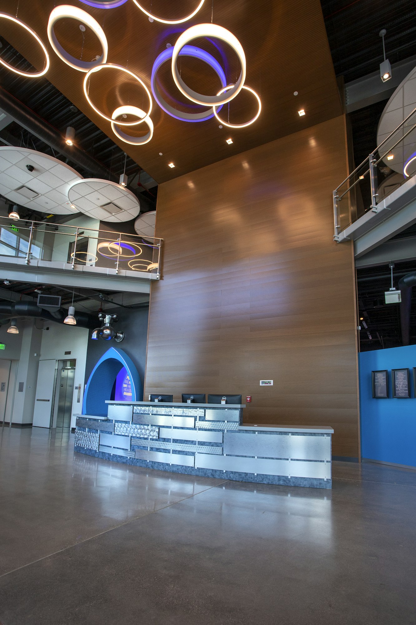 Modern lobby with circular ceiling lights, metal and wood decor, reception desk, and a balcony.