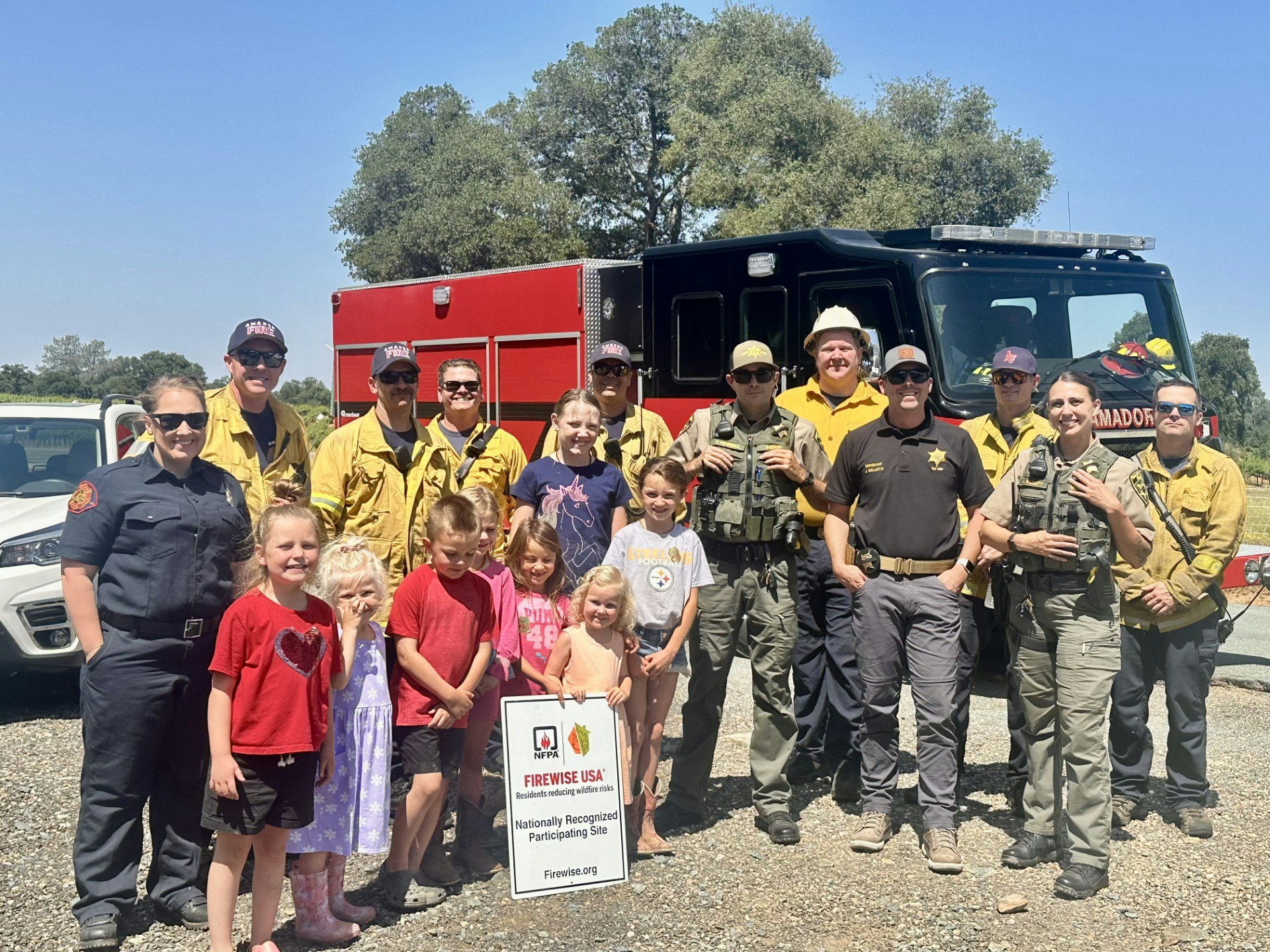 A group of emergency responders and children pose in front of a fire truck and sign for Firewise USA.