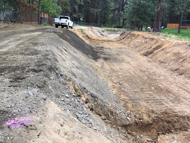 A partially excavated area with dirt mounds and a white truck in a wooded setting.