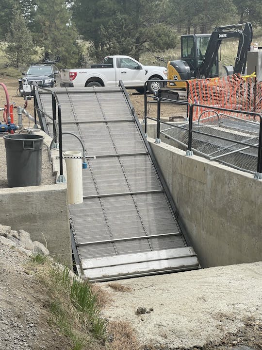 Construction site with an excavator, truck, and safety barriers under an overpass. (Sideways image)