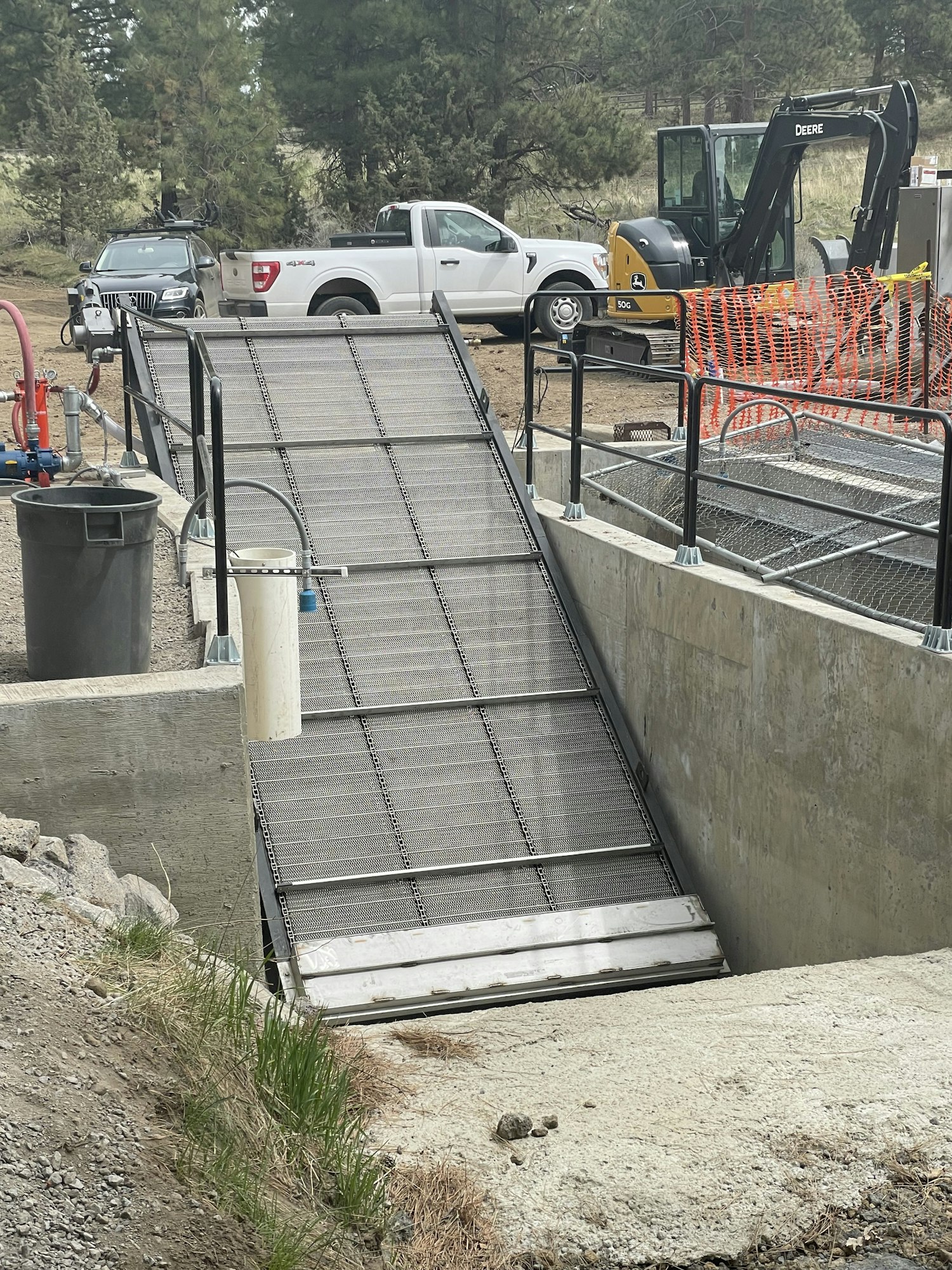 Construction site with an excavator, truck, and safety barriers under an overpass. (Sideways image)