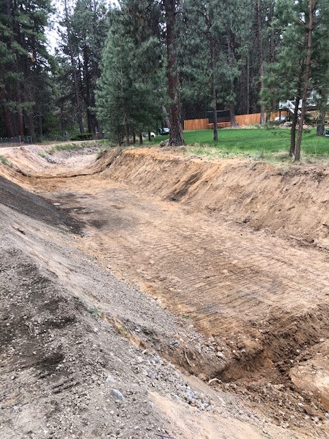 A cleared dirt area in a forested environment, surrounded by trees, showing signs of excavation or grading work.