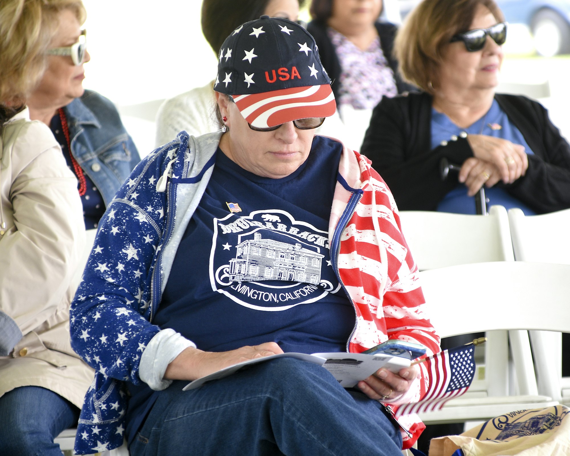 Person wearing USA-themed apparel checking their phone, seated among other individuals.