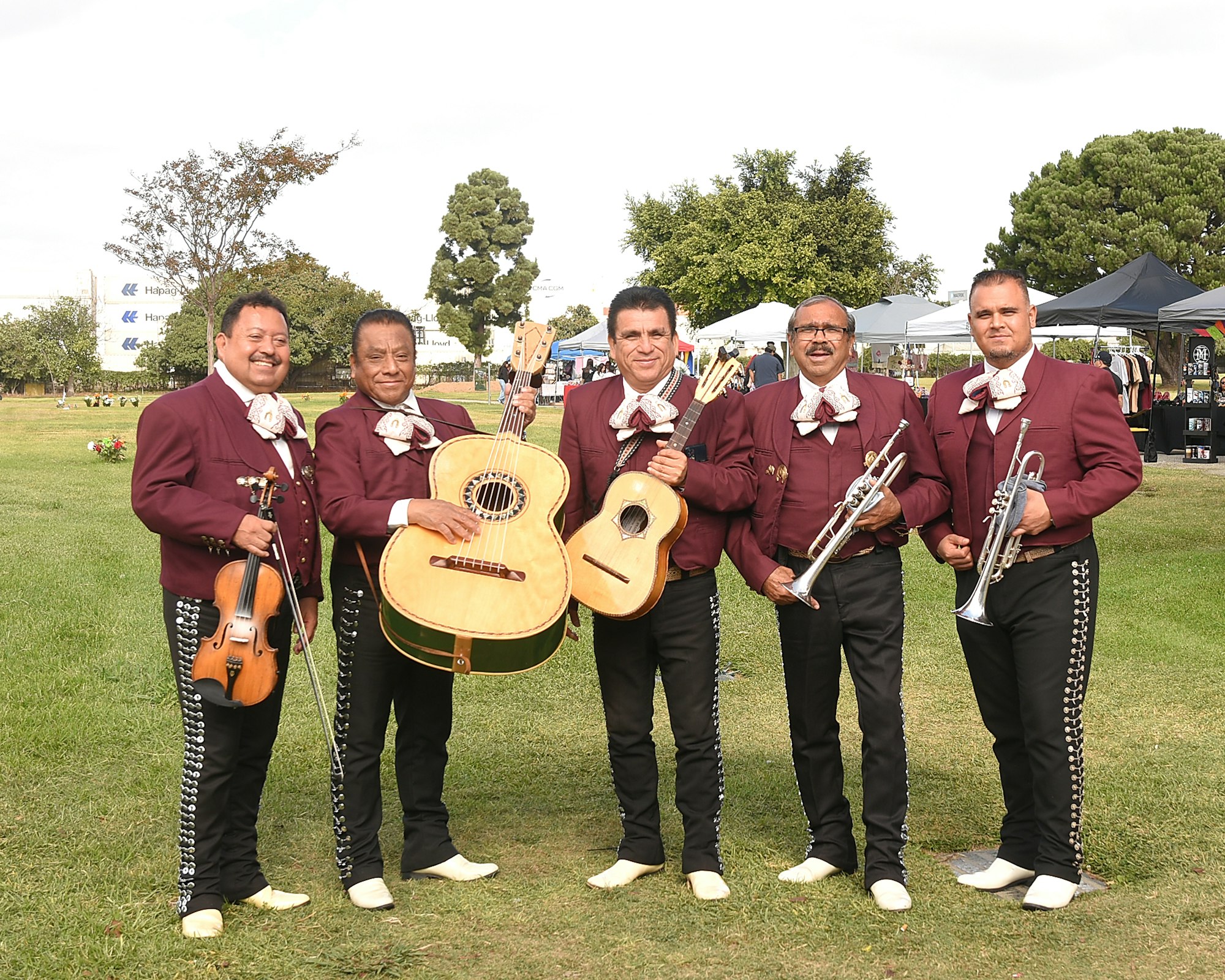A mariachi band with violins, guitars, and trumpets, dressed in traditional attire, posing outdoors.