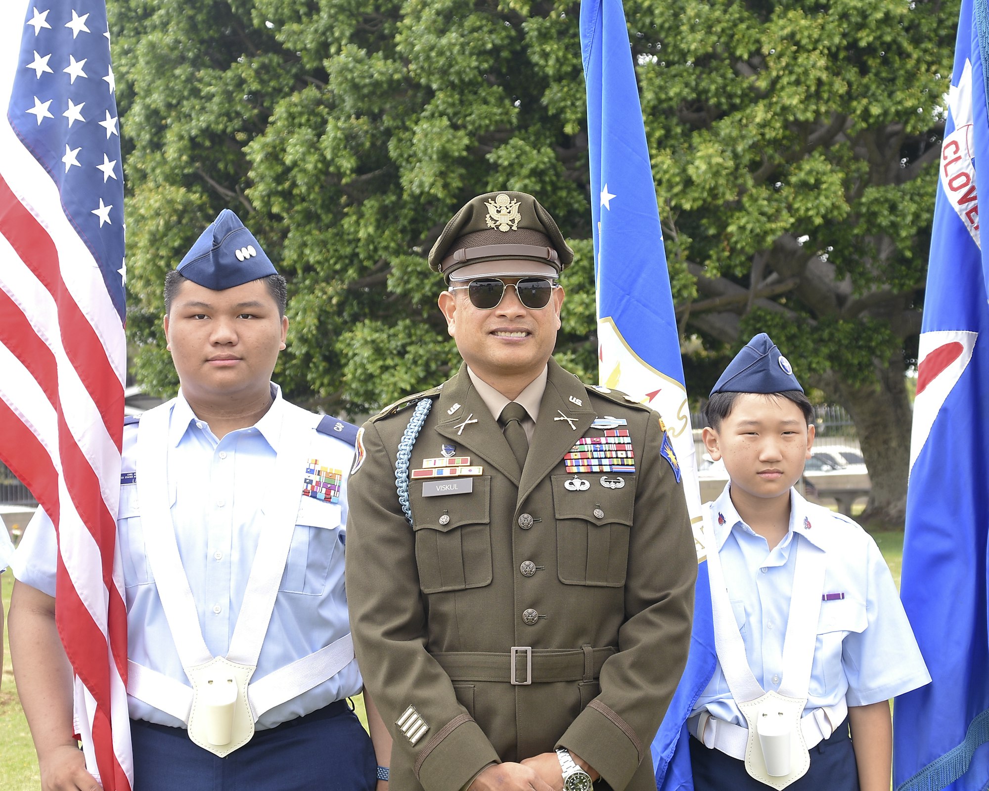 Three cadets in uniform with American flag and military flags.