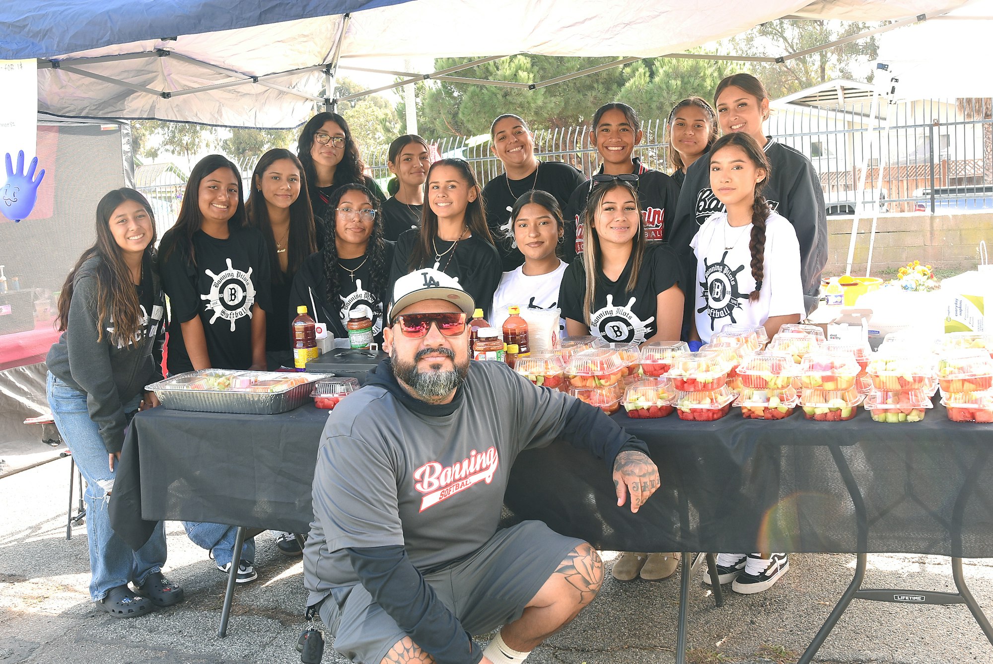A group of happy people posing behind a table with fruit cups at an outdoor event.