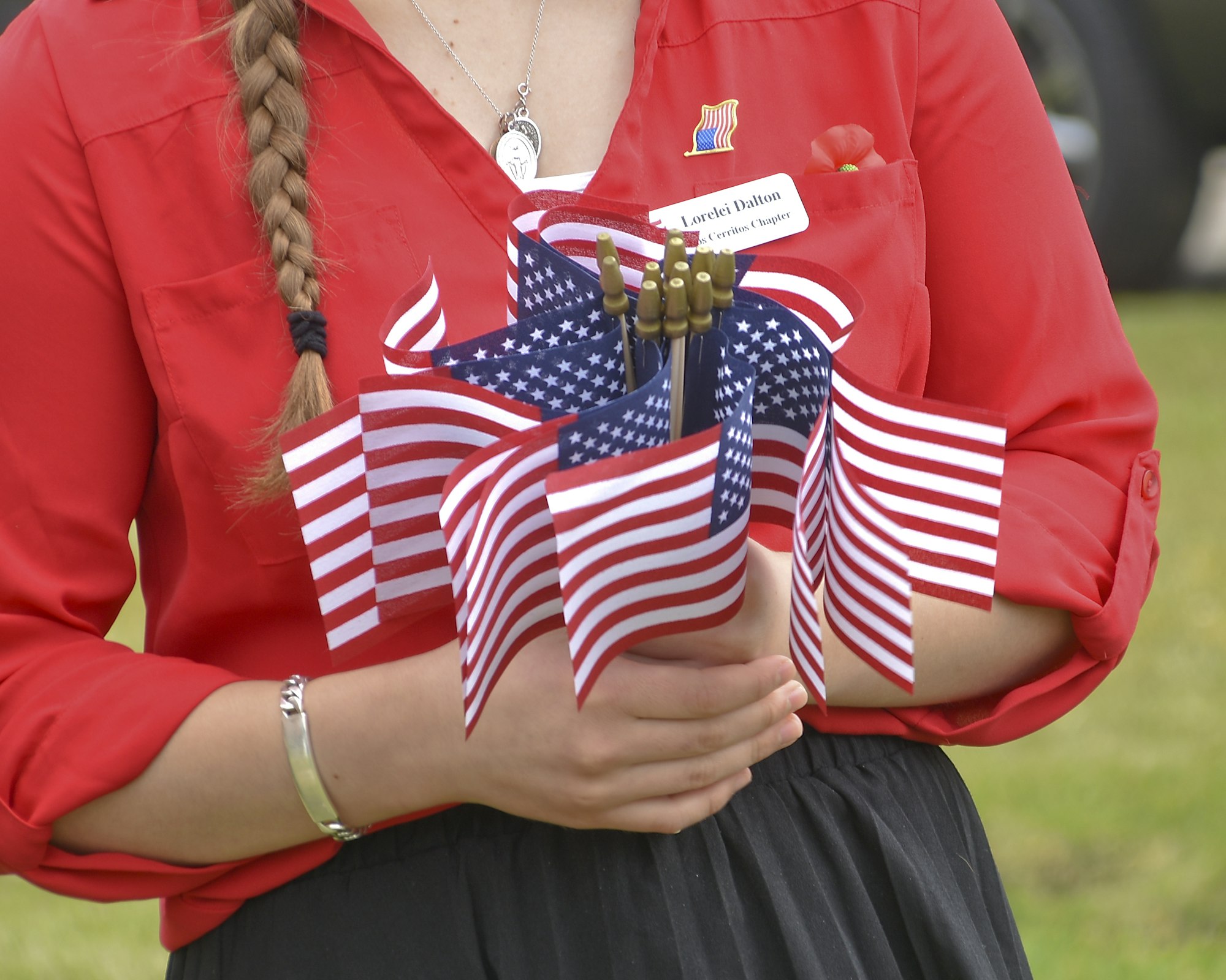 Person holding multiple small American flags and wearing a red blouse.