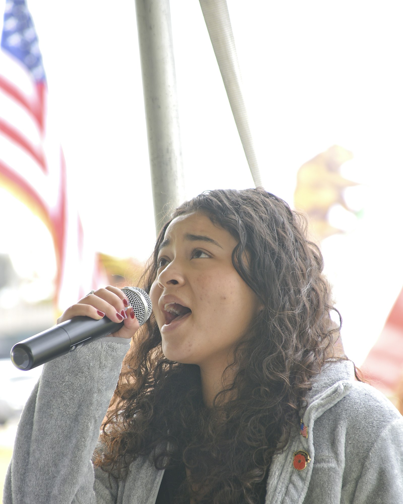 A person singing into a microphone with an American flag in the background.