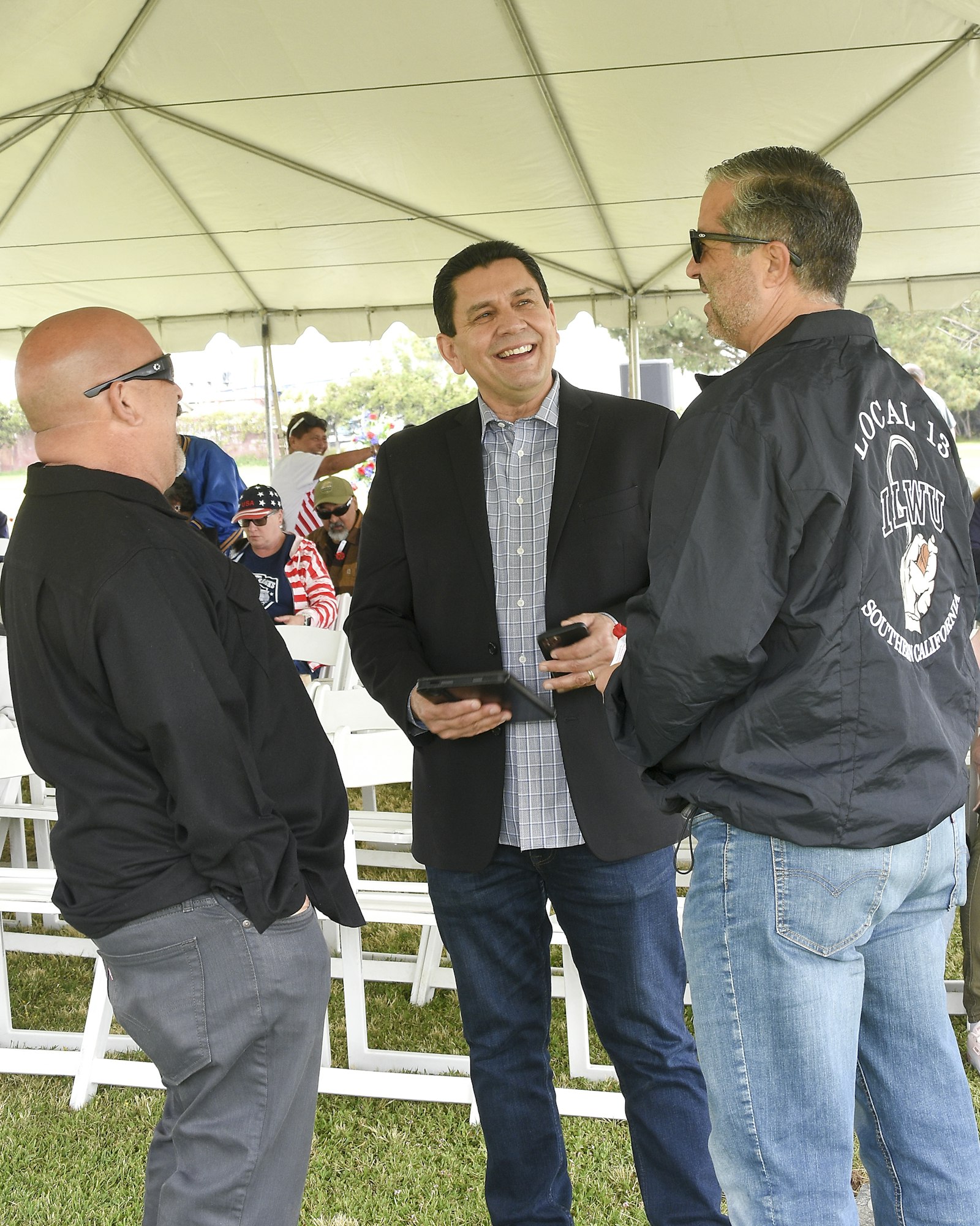 Three men are conversing under a tent; one is laughing.