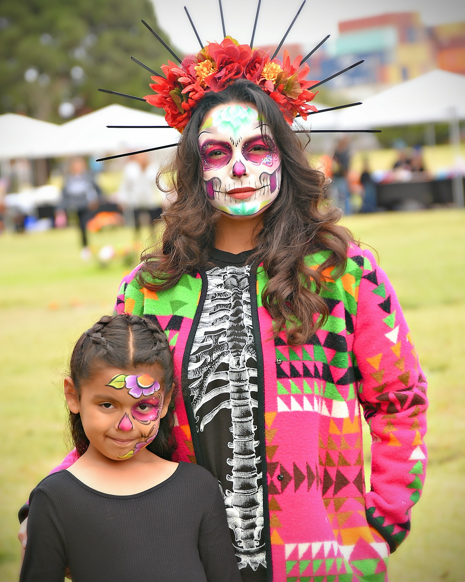 Two people with face paint, one with a detailed skull makeup and floral headpiece, likely celebrating Día de los Muertos.