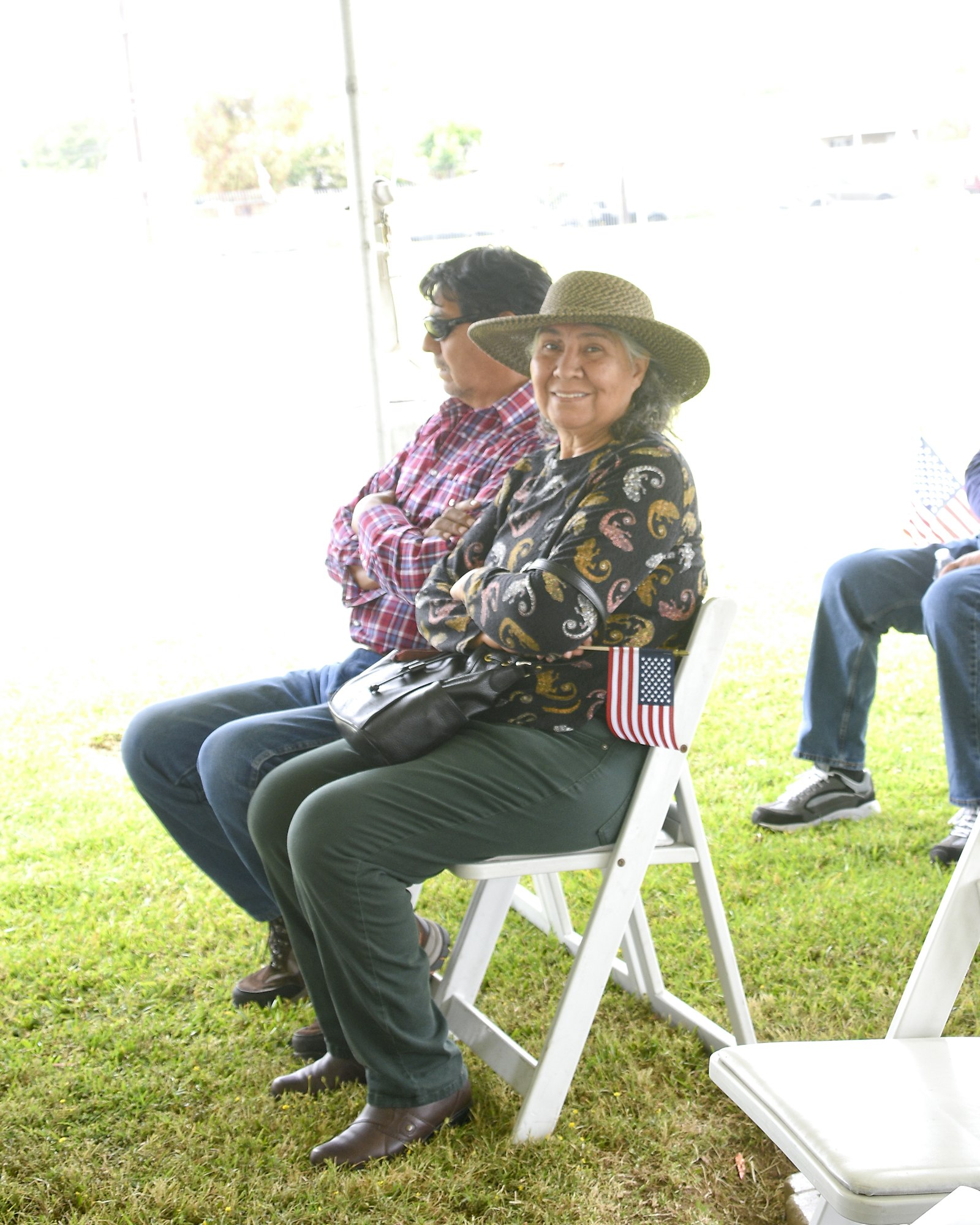 Two people sitting on chairs outdoors, one smiling at the camera. Bright daylight.