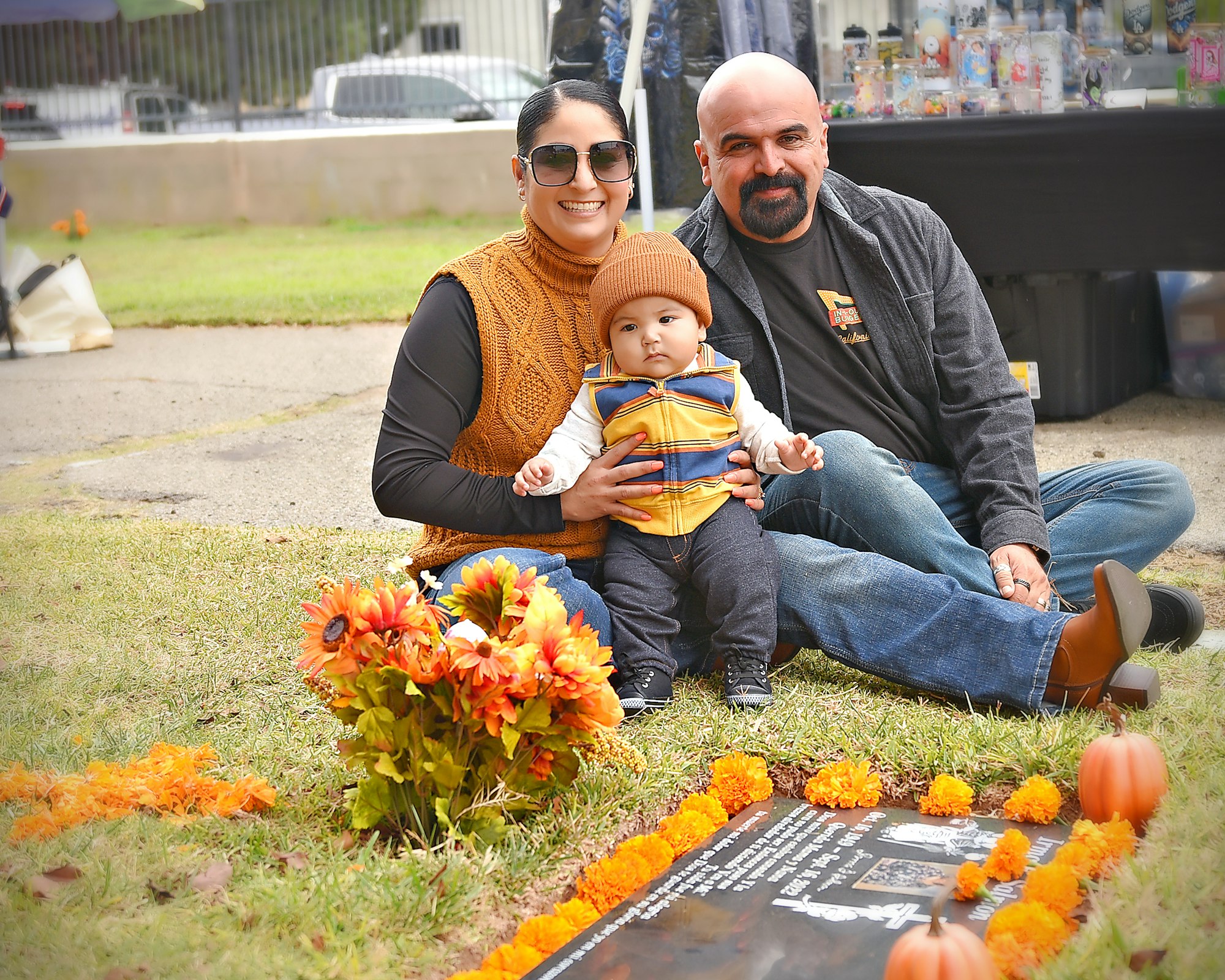 A family posing with a baby, sitting by a decorated gravesite with flowers and vibrant colors.